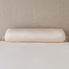 Paloma Throw Pillow | Pearl | bolster on white sheets with a neutral headboard.