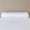 Paloma Throw Pillow | White | bolster on white sheets with a neutral headboard.