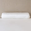Paloma Throw Pillow | Winter White | bolster on white sheets with a neutral headboard.