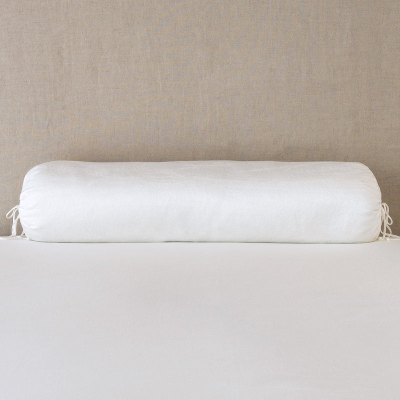 Paloma Throw Pillow | Winter White | bolster on white sheets with a neutral headboard.