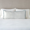 Paloma Throw Pillow | Cloud | 16x36 charmeuse pllow wth silk velvet trim against white sleeping pillows and sheets — straight on with neutral background.