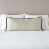 Paloma Throw Pillow | Fog | 16x36 charmeuse pllow wth silk velvet trim against white sleeping pillows and sheets — straight on with neutral background.