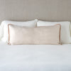 Paloma Throw Pillow | Pearl | 16x36 charmeuse pllow wth silk velvet trim against white sleeping pillows and sheets — straight on with neutral background.