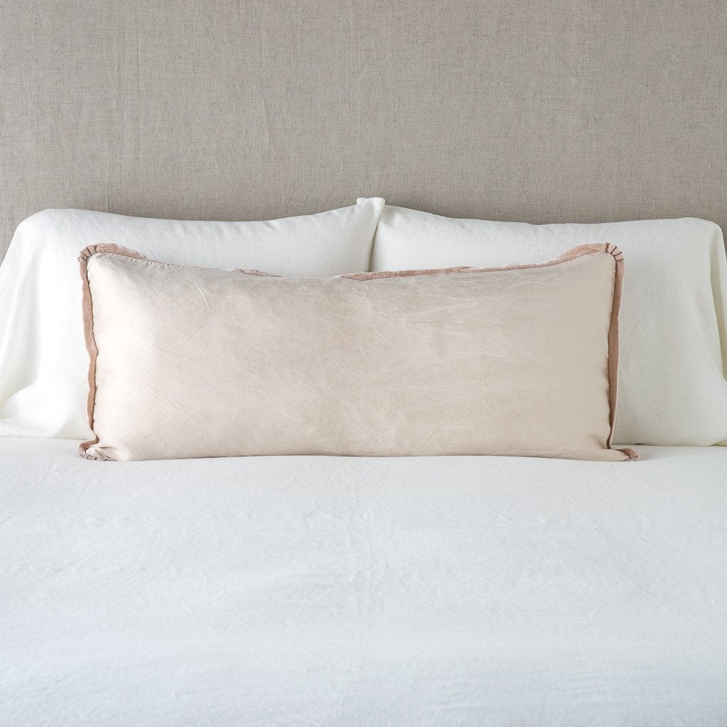 Paloma Throw Pillow | Pearl | 16x36 charmeuse pllow wth silk velvet trim against white sleeping pillows and sheets — straight on with neutral background.
