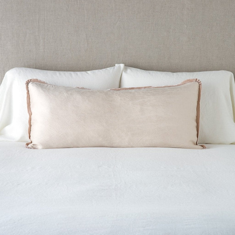 Paloma Throw Pillow | Pearl | 16x36 charmeuse pllow wth silk velvet trim against white sleeping pillows and sheets — straight on with neutral background.