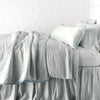 Paloma Blanket | Cloud | throw blanket rumpled on a charmeuse monochromatic bed - side view.