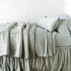 Paloma Blanket | Paloma throw blanket rumpled on a charmeuse monochromatic bed - eucalyptus, side view.