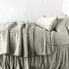 Paloma Blanket | Fog | throw blanket rumpled on a charmeuse monochromatic bed - side view.