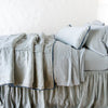 Paloma Blanket | Mineral | throw blanket rumpled on a charmeuse monochromatic bed - side view.