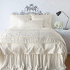 Paloma Blanket | Parchment | throw blanket folded at the end of a monochromatic, charmeuse bed - end of bed view.