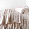Paloma Blanket | Pearl | Paloma throw blanket rumpled on a charmeuse monochromatic bed - pearl, side view.