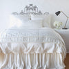 Paloma Blanket | Winter White | throw blanket folded at the end of a monochromatic, charmeuse bed - end of bed view.