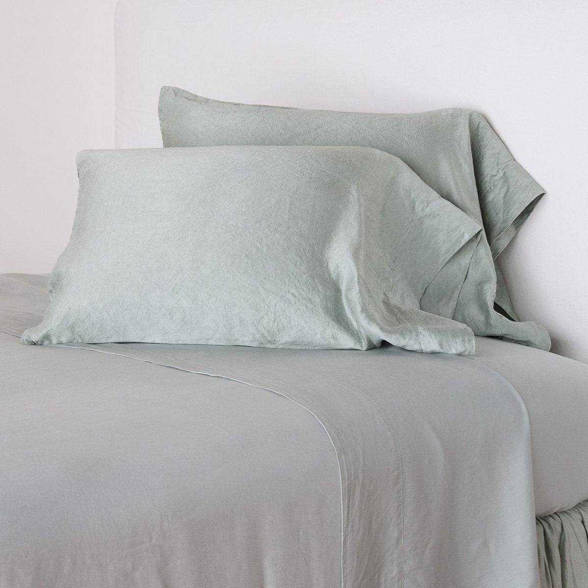 Paloma Pillowcase (Single) | Mineral | Paloma sleeping pillows leaning upright against a white wall on monochromatic sheeting - mineral, cropped three-quarter angle.