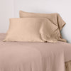 Paloma Pillowcase (Single) | Rouge | sleeping pillows leaning upright against a white wall on monochromatic sheeting - cropped three-quarter angle.