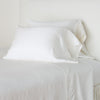 Paloma Pillowcase (Single) | Winter White | Paloma sleeping pillows leaning upright against a white wall on monochromatic sheeting - winter white, cropped three-quarter angle.
