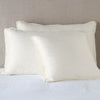 Paloma Sham | Parchment | shams leaning upright on white sheeting against a neutral headboard.