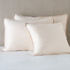 Paloma Sham | Pearl | shams leaning upright on white sheeting against a neutral headboard.
