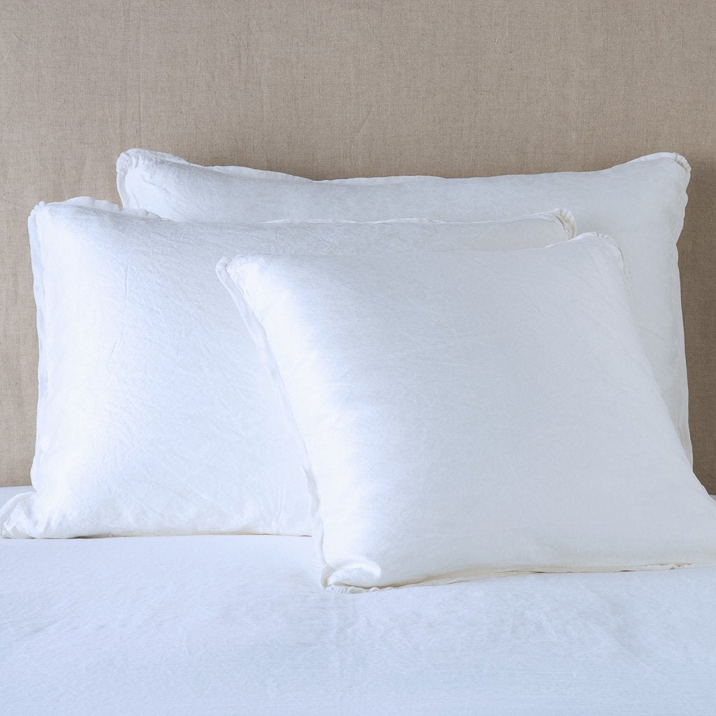 Paloma Sham | White | shams leaning upright on white sheeting against a neutral headboard.