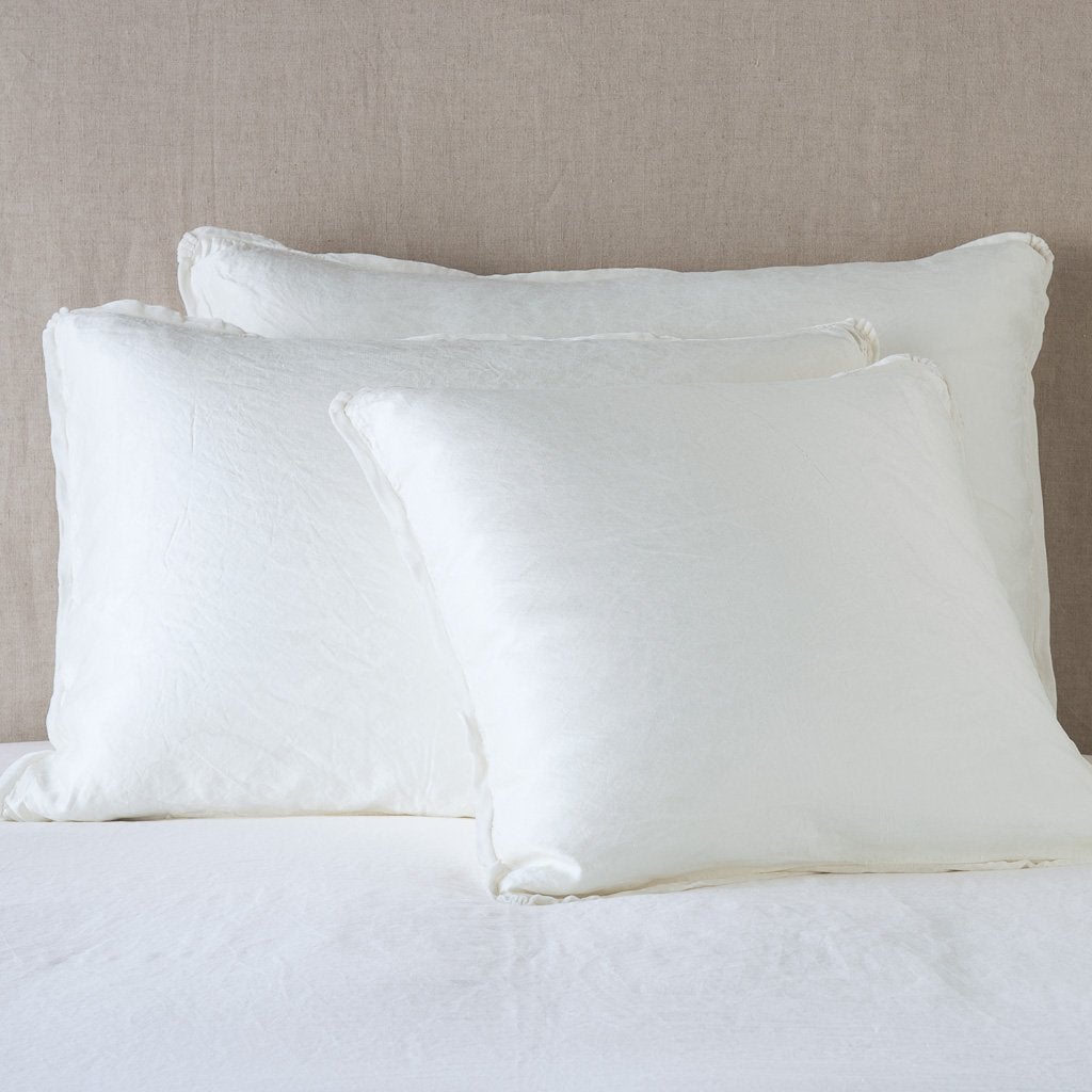 Paloma Sham | Winter White | shams leaning upright on white sheeting against a neutral headboard.