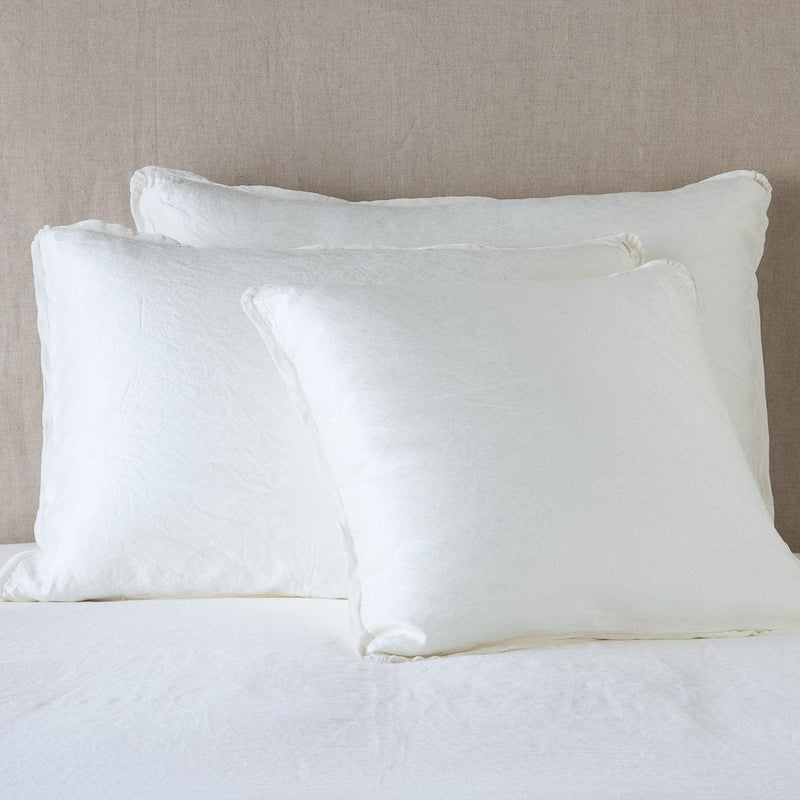 Paloma Sham | Winter White | shams leaning upright on white sheeting against a neutral headboard.