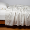 Seraphina Flat Sheet | Winter White | rumpled flat sheet with matching fitted sheet and sleeping pillow - side view.