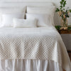Silk velvet quilted coverlet on a neatly made, winter white bed - end of bed view.