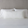 Silk Velvet Quilted Throw Pillow | Winter White | 16x36 pillow leaning upright against white sleeping pillows and a neutral headboard.