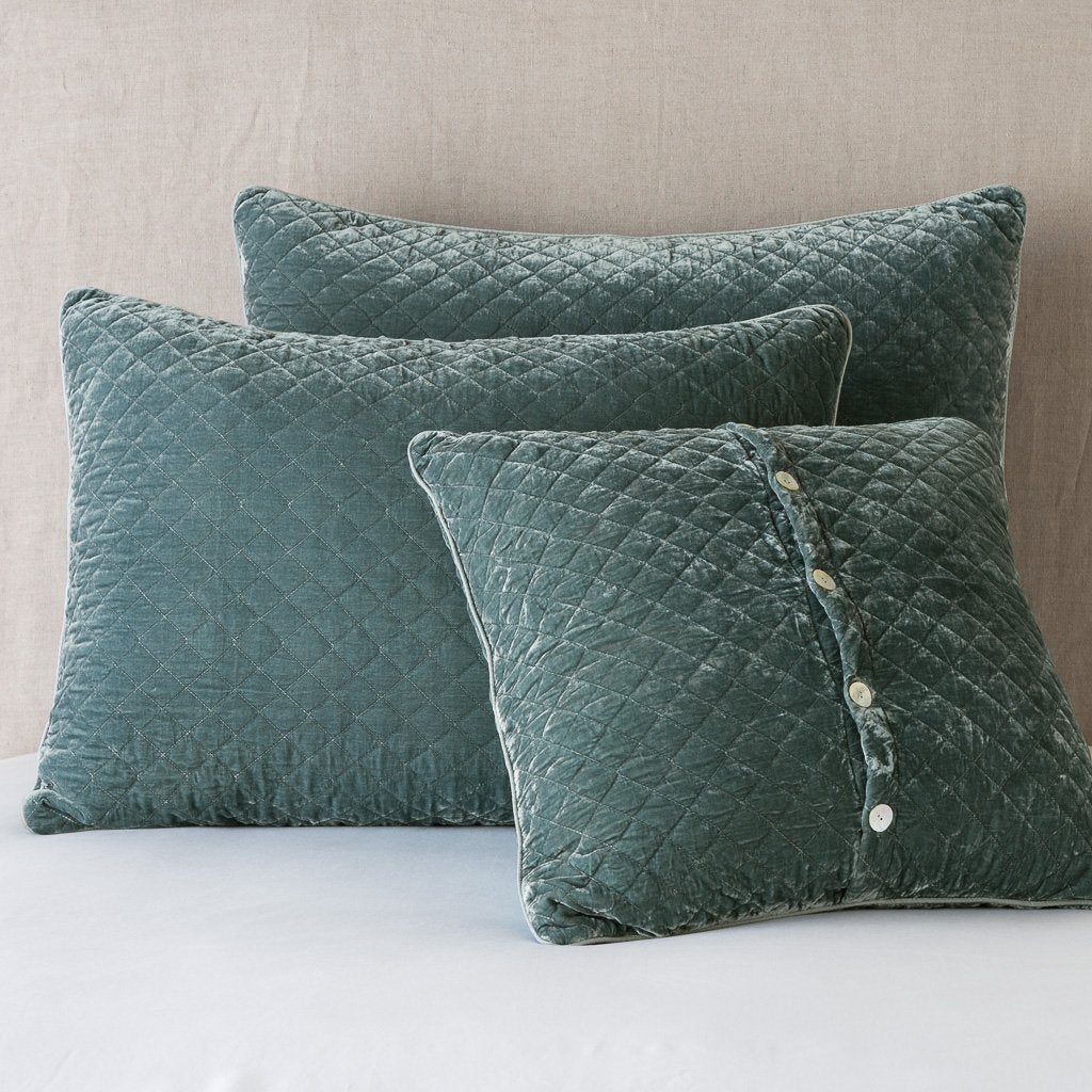 Silk Velvet Quilted Sham | Eucalyptus | shams leaning upright against a neutral headboard. One sham is backwards to showcase the shimmering shell button closure.