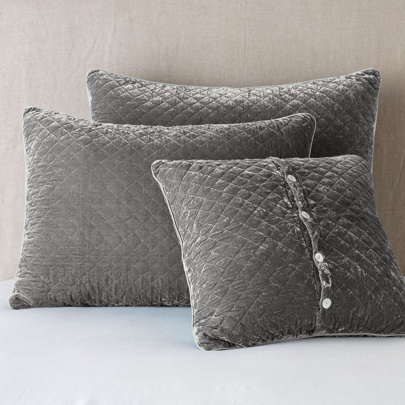 Silk Velvet Quilted Sham | Fog | shams leaning upright against a neutral headboard. One sham is backwards to showcase the shimmering shell button closure.