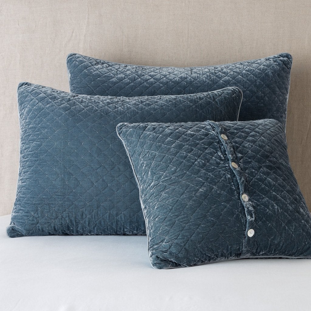 Silk Velvet Quilted Sham | Mineral | shams leaning upright against a neutral headboard. One sham is backwards to showcase the shimmering shell button closure.