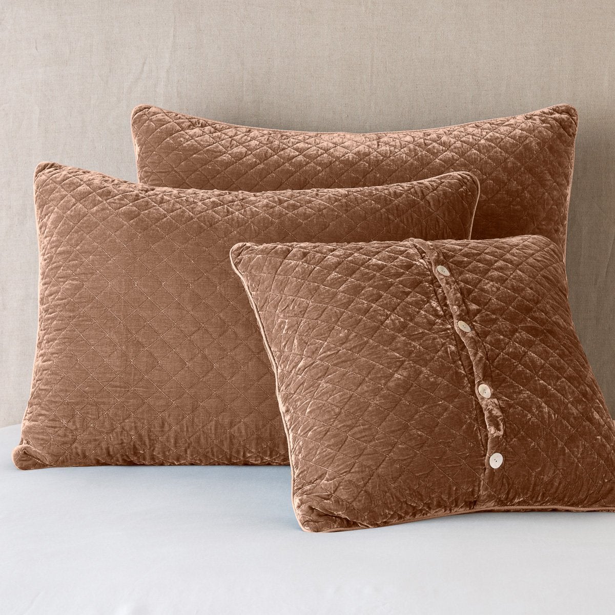 Silk Velvet Quilted Sham | Rouge | shams leaning upright against a neutral headboard. One sham is backwards to showcase the shimmering shell button closure.