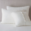 Silk Velvet Quilted Sham | Winter White | shams leaning upright against a neutral headboard. One sham is backwards to showcase the shimmering shell button closure.