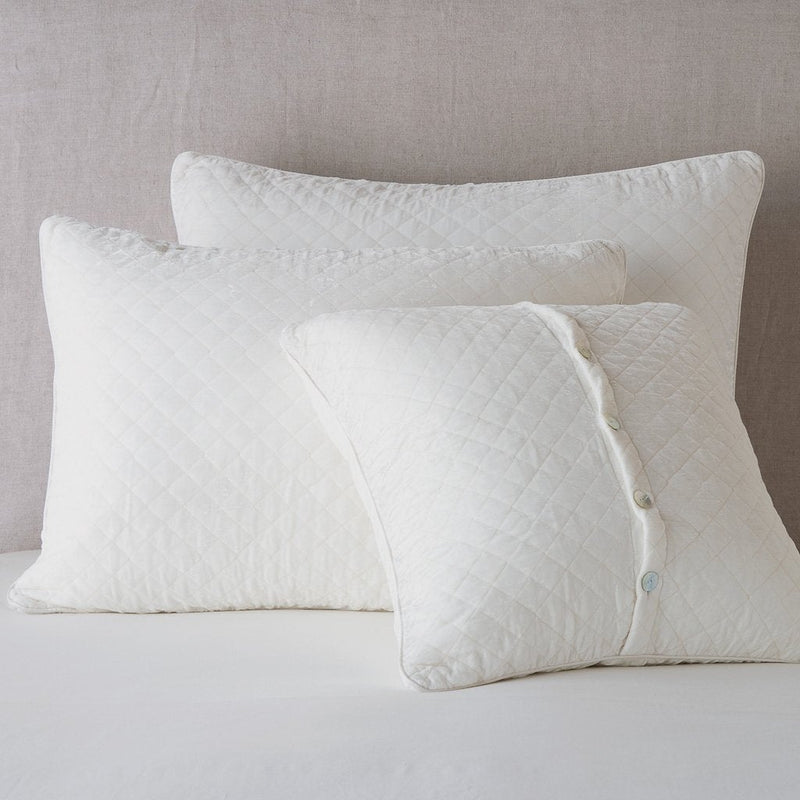 Silk Velvet Quilted Sham | Winter White | shams leaning upright against a neutral headboard. One sham is backwards to showcase the shimmering shell button closure.