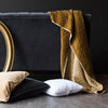 Silk Velvet Quilted Blanket | Silk velvet throw blanket in honeycomb, draped over the back on a dark grey couch. A gold oval frame is partially visible, complementing the rich gold of the blanket.