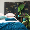 Silk Velvet Quilted Blanket | Cenote | Silk velvet quilted coverlet in cenote draped over the end of a pearl bed. Dark floral wall panel, blue-green ceramic vases, and big green plants complement the rich silk velvet - cropped three-quarter angle.