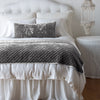 Silk Velvet Quilted Blanket | Fog | throw blanket and matching lumbar pillow on a neatly made white bed - end of bed view.