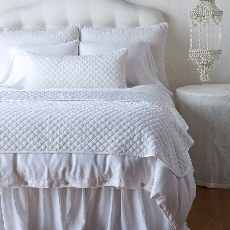 Silk Velvet Quilted Blanket | White | throw blanket and matching lumbar pillow on a neatly made white bed - end of bed view.