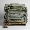 Taline Blanket | stack of three blankets shows colors, textures and tassels. Blankets shown in Eucalyptus, Cloud and Fog against a white background