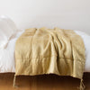 Taline Blanket | Honeycomb | Taline throw blanket draped over a white bed - honeycomb, side view.