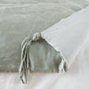 Taline Blanket | Mineral | Close up of blanket, with a corner turned back to showcase the midweight linen back and corner tassel - overhead view.
