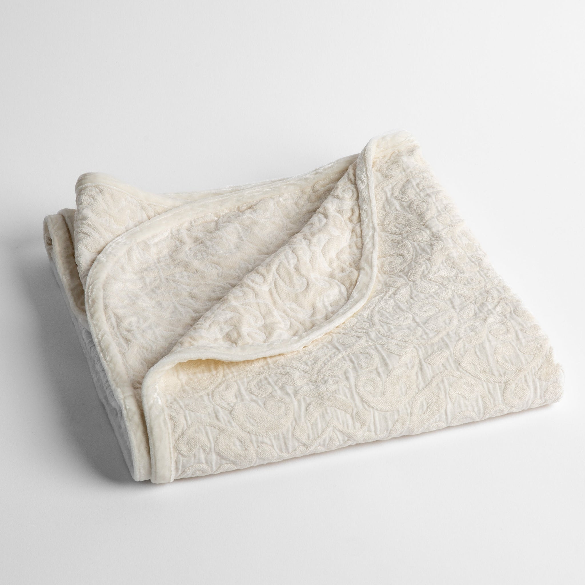 Vienna Baby Blanket | Winter White | a folded cotton chenille baby blanket trimmed in silk velvet shot overhead at a slight angle against a white background.