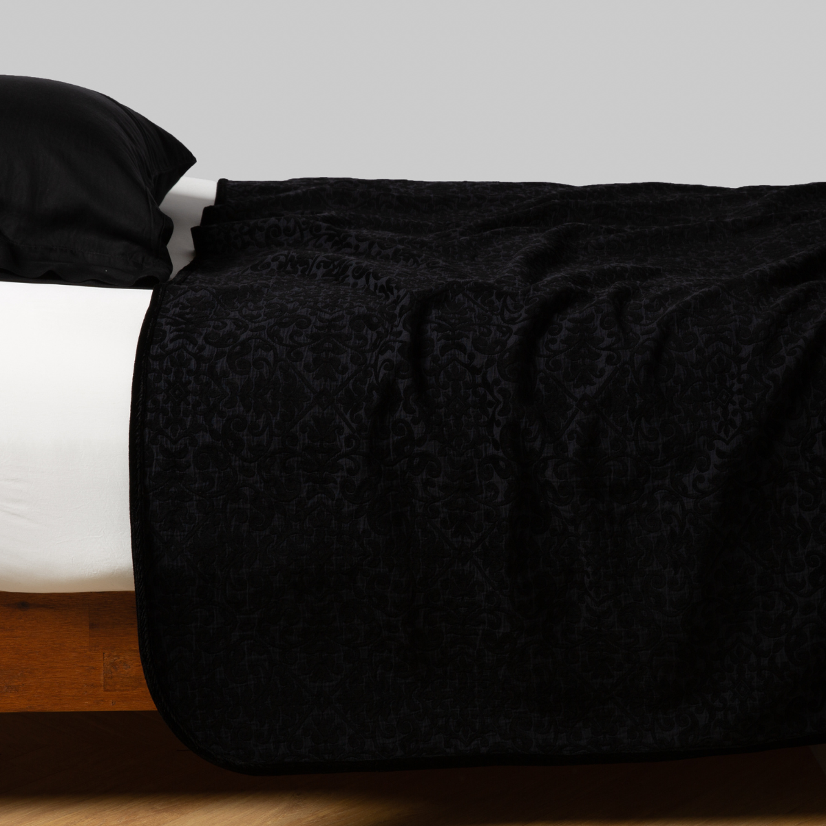 Vienna Coverlet | Corvino | coverlet neatly arranged on white sheeting with matching sleeping pillow - side view.