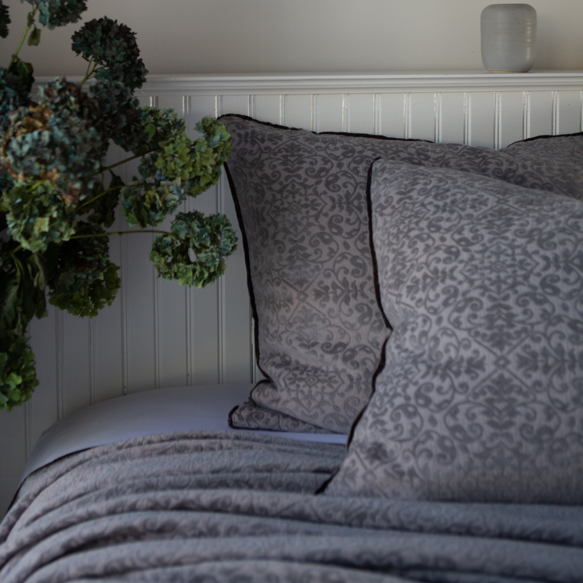 Moonlight | Vienna shams and coverlet in moonlight against a white beadboard wall. Cropped head-on angle showcases silk velvet trim detail.