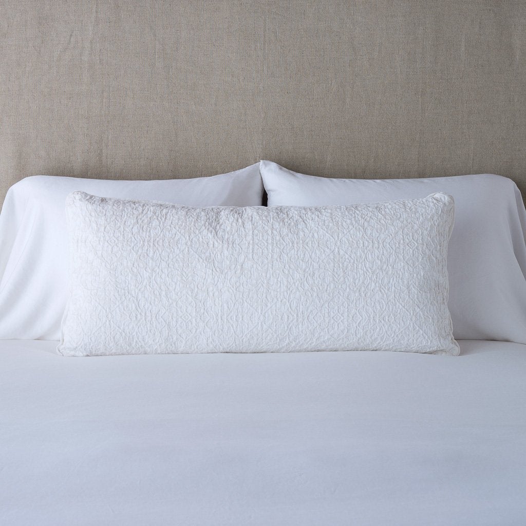 Vienna Throw Pillow | White | 16x36 pillow leaning upright against white sleeping pillows on a neutral headboard.