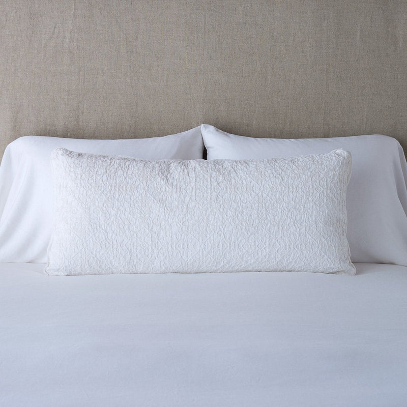 Vienna Throw Pillow | White | 16x36 pillow leaning upright against white sleeping pillows on a neutral headboard.